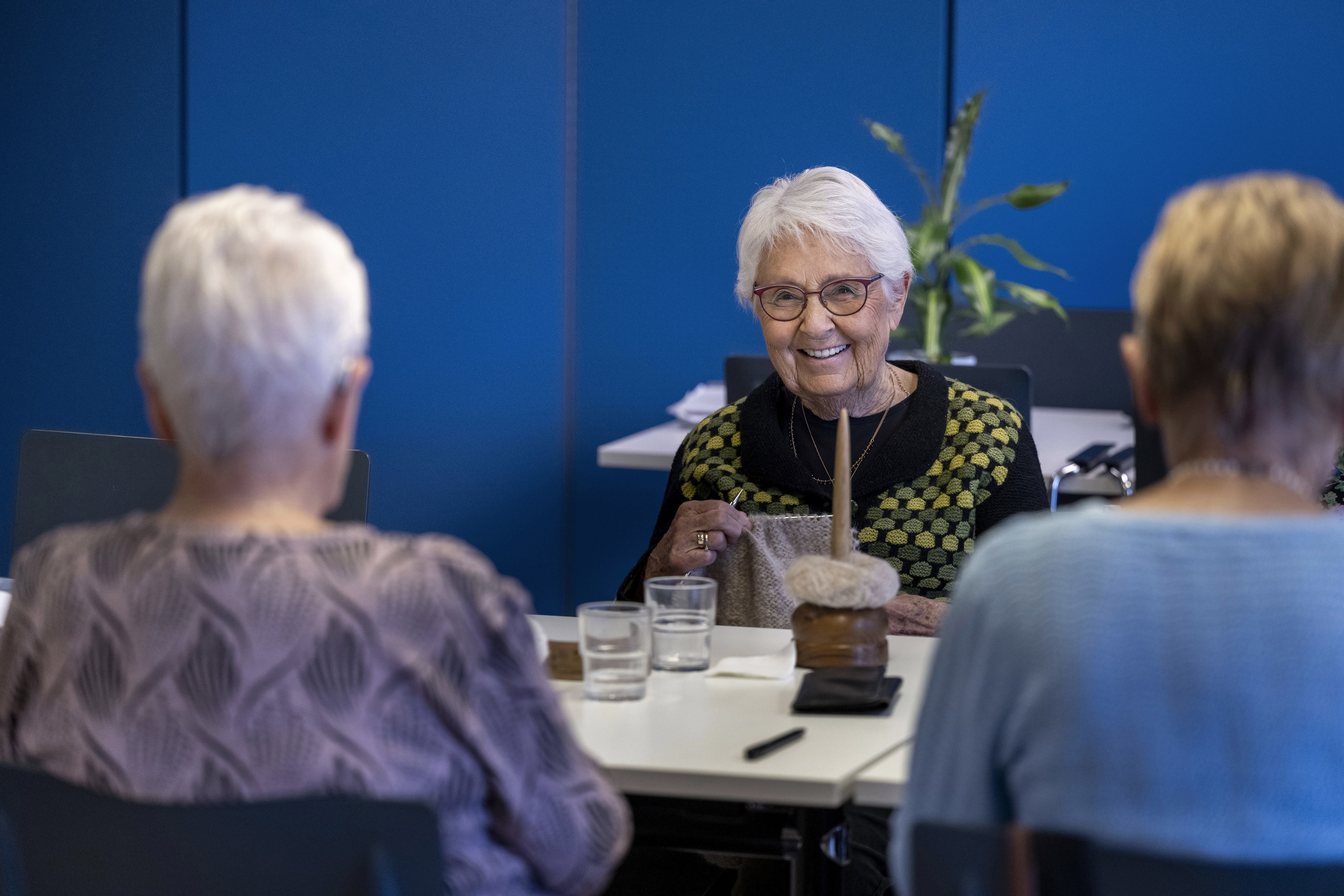 Tre damer sidder ved et bord og laver håndarbejde
